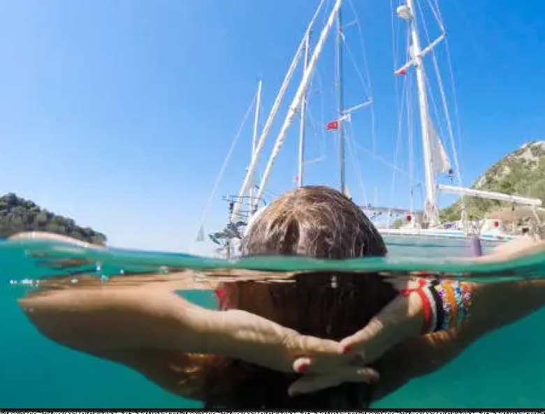 Swimmer floating beside a sailing yacht